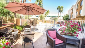 A patio area with wicker furniture, a large umbrella, and a pool in the background. - Sleep Inn North Scottsdale near Mayo Clinic (Scottsdale)