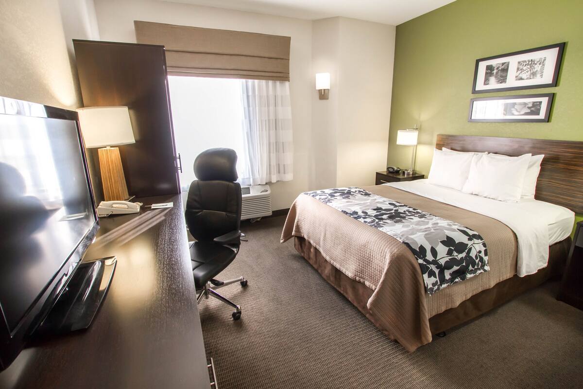 Habitación de hotel con cama, escritorio, silla, televisión y ventana con cortinas.