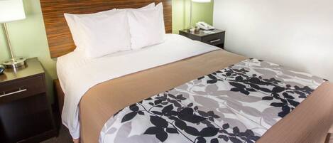 A neatly made bed with white linens and a floral-patterned duvet, a bedside lamp, a nightstand with a phone, and framed pictures on the wall.