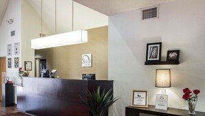 A hotel reception area with a reception desk, a large mirror, framed pictures on the wall, a potted plant, and a welcome mat. - Sleep Inn North Scottsdale near Mayo Clinic (Scottsdale)