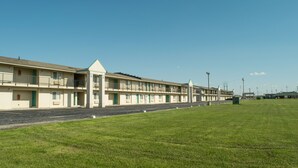 A motel with a row of rooms, a grassy parking lot, and a clear blue sky. - Regency Inn Perrysburg (Perrysburg)