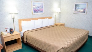 A hotel room with a wooden bed, a nightstand with a phone and a remote, two wall-mounted lamps, and two framed pictures on the wall. - Regency Inn Perrysburg (Perrysburg)
