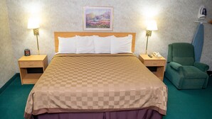 A hotel room with a large bed, two bedside tables, a green armchair, a painting on the wall, and a telephone on one of the tables. - Regency Inn Perrysburg (Perrysburg)