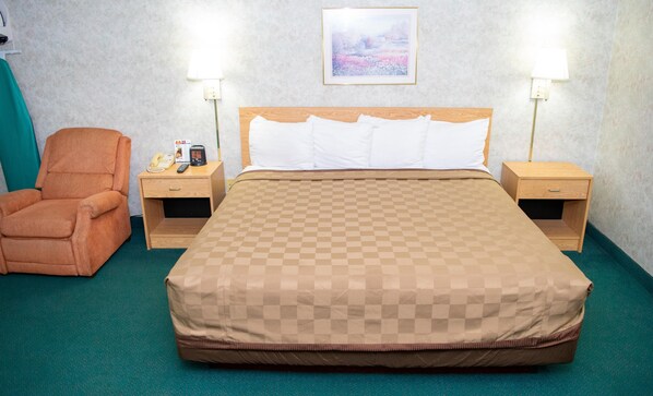 A hotel room with a large bed, two bedside tables, a chair, and a wall-mounted picture.