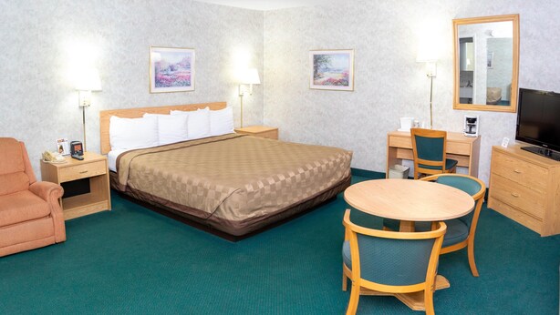 A hotel room with a bed, a desk with a chair, a sofa, and a television. - Regency Inn Perrysburg (Perrysburg)