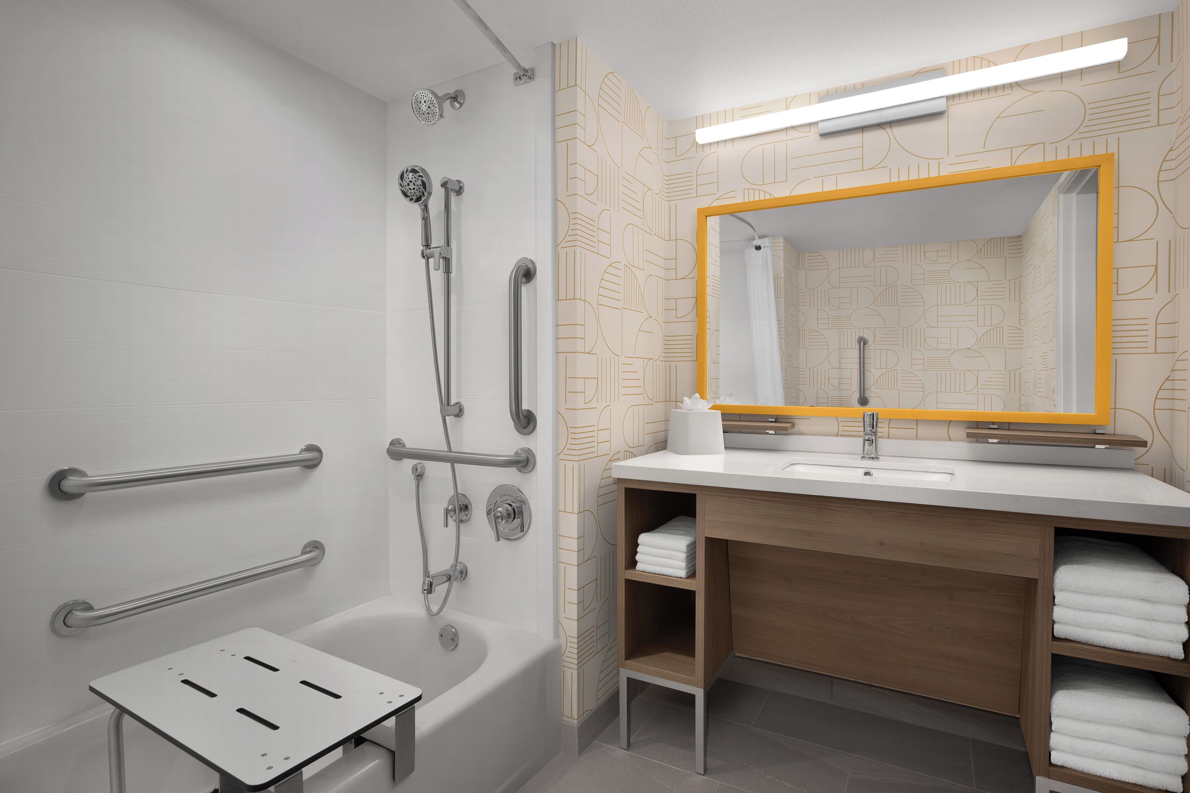 Un baño moderno con ducha, barras de apoyo, lavamanos y espejo con marco amarillo.