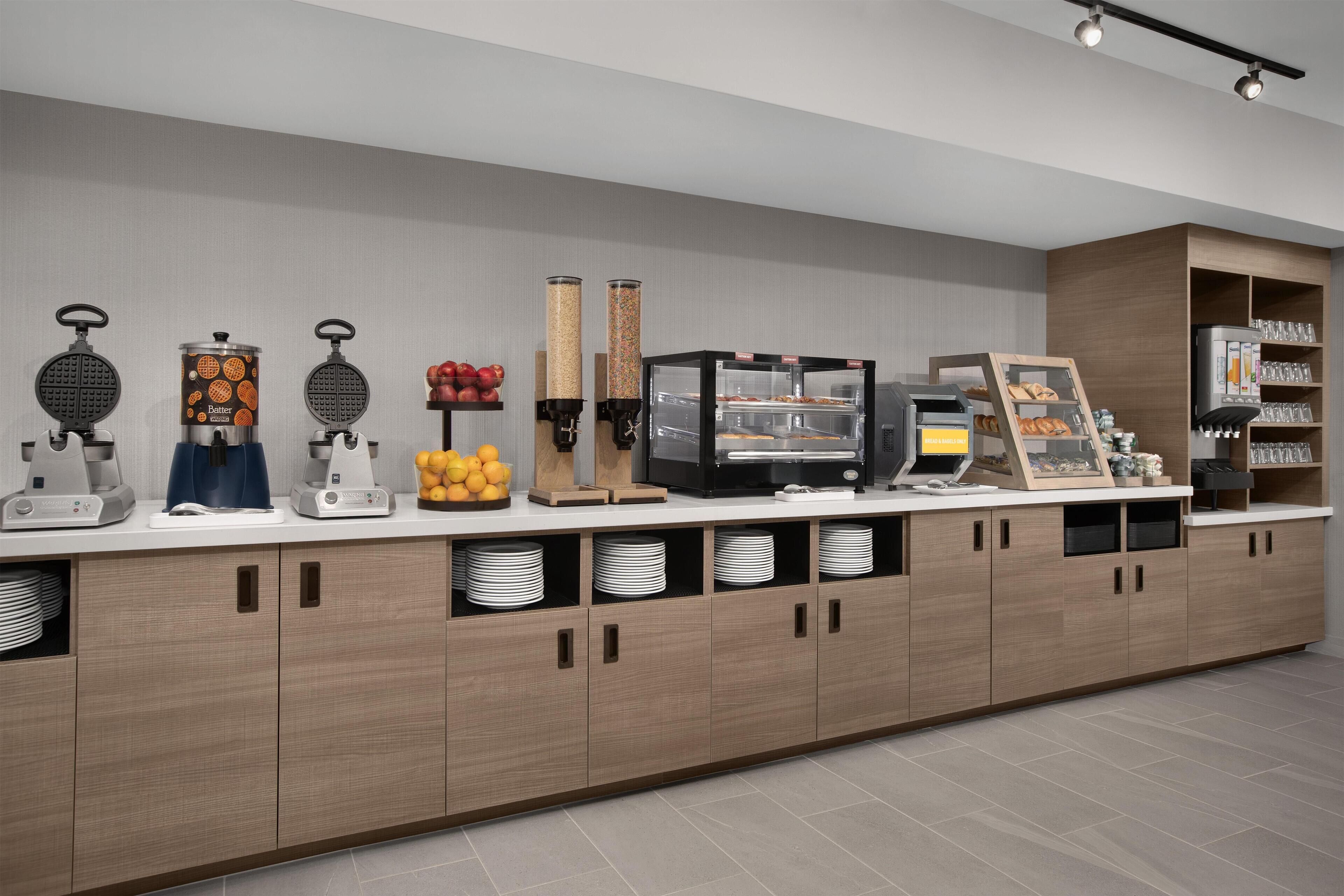 A breakfast bar with waffle makers, a coffee machine, and a fruit display.