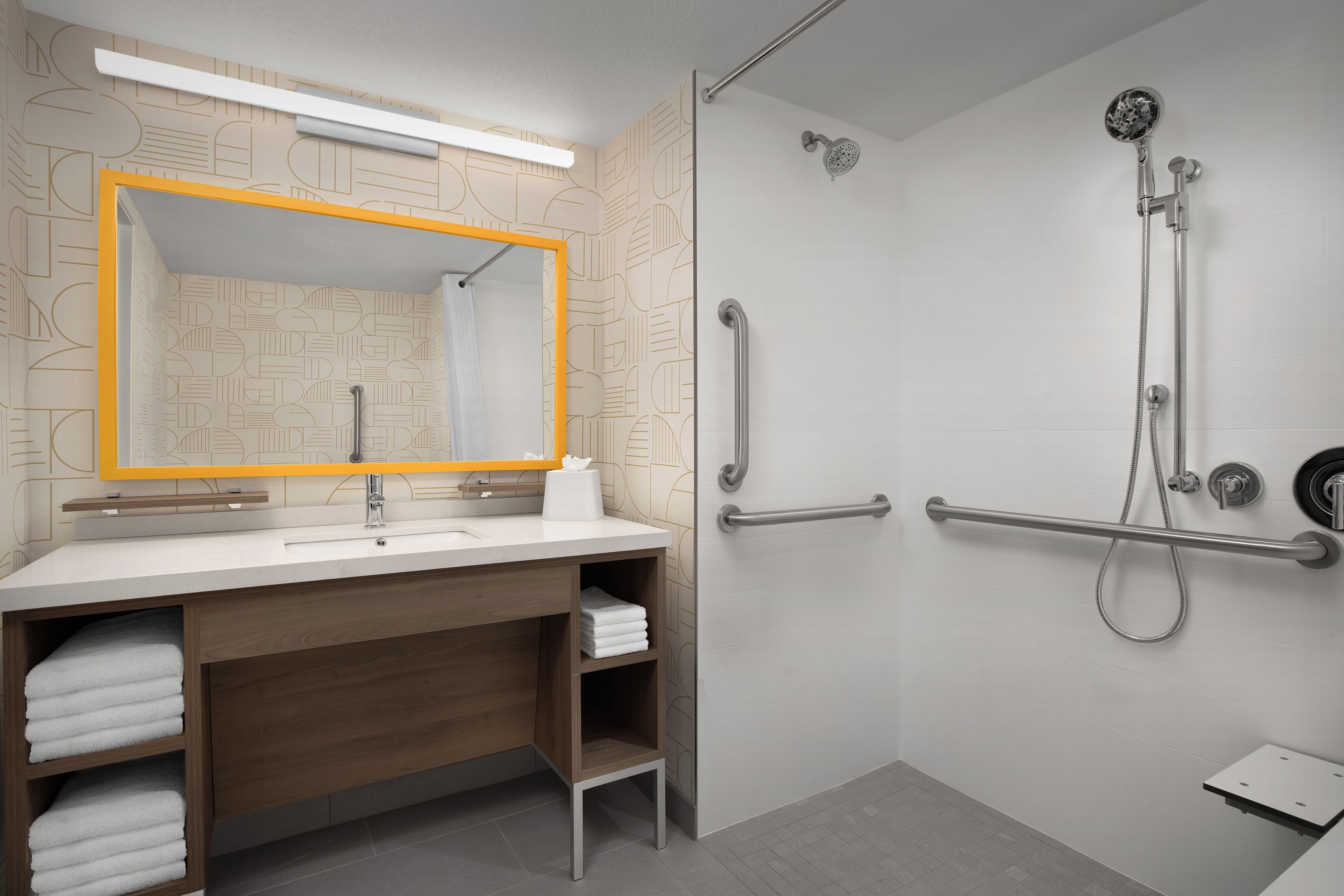 A modern bathroom with a large mirror, a shower with a handheld showerhead, and a grab bar.