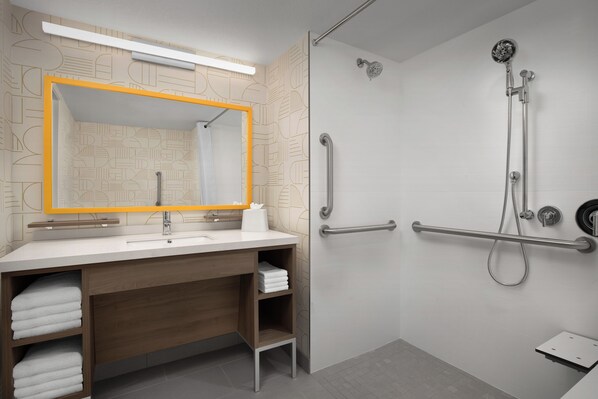 Ein modernes Badezimmer mit einem großen Spiegel, einer Dusche inklusive Handbrause und einer Haltestange.
