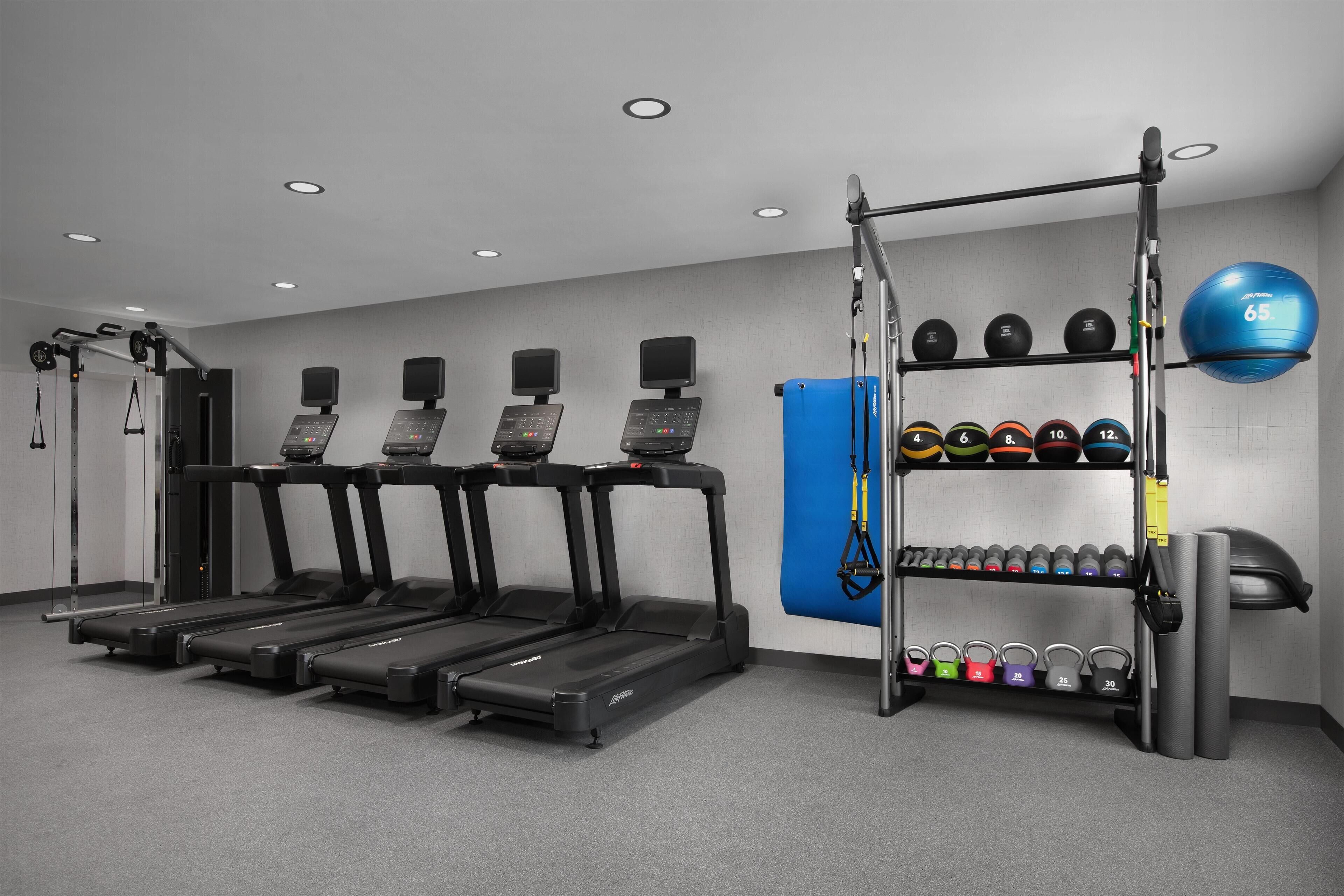 Une salle de sport équipée de tapis de course, d’appareils de musculation et d’un ensemble de haltères et de balles lestées.