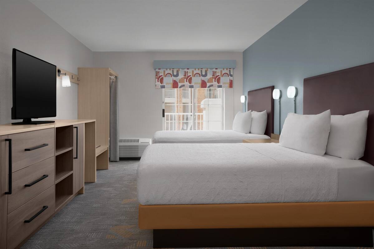 A hotel room with two beds, a TV, a wardrobe, and a window with curtains.