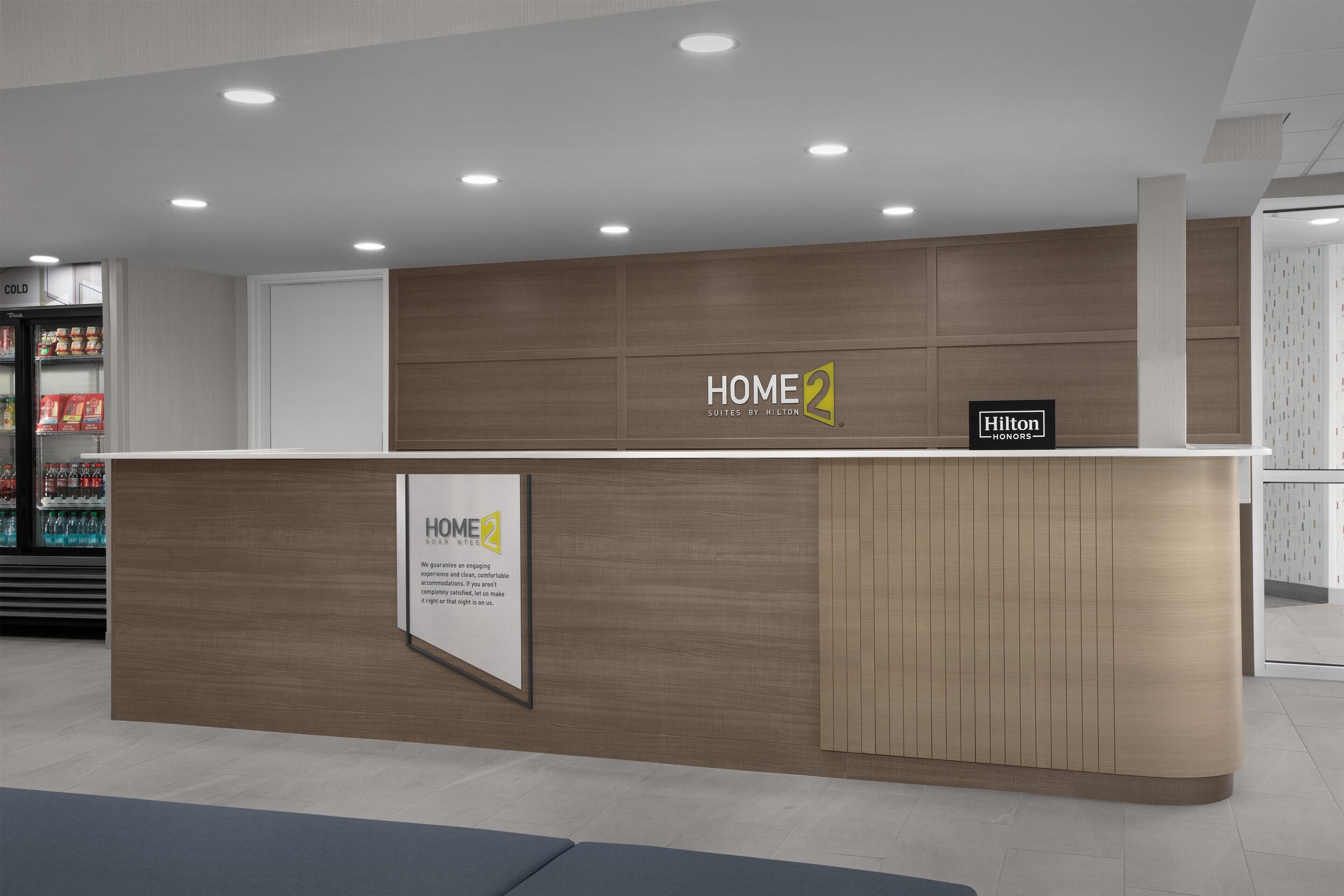 A reception desk with a wooden finish and a sign reading "HOME2 Suites by Hilton".