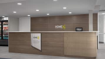 A reception desk with a wooden finish and a sign reading "HOME2 Suites by Hilton".