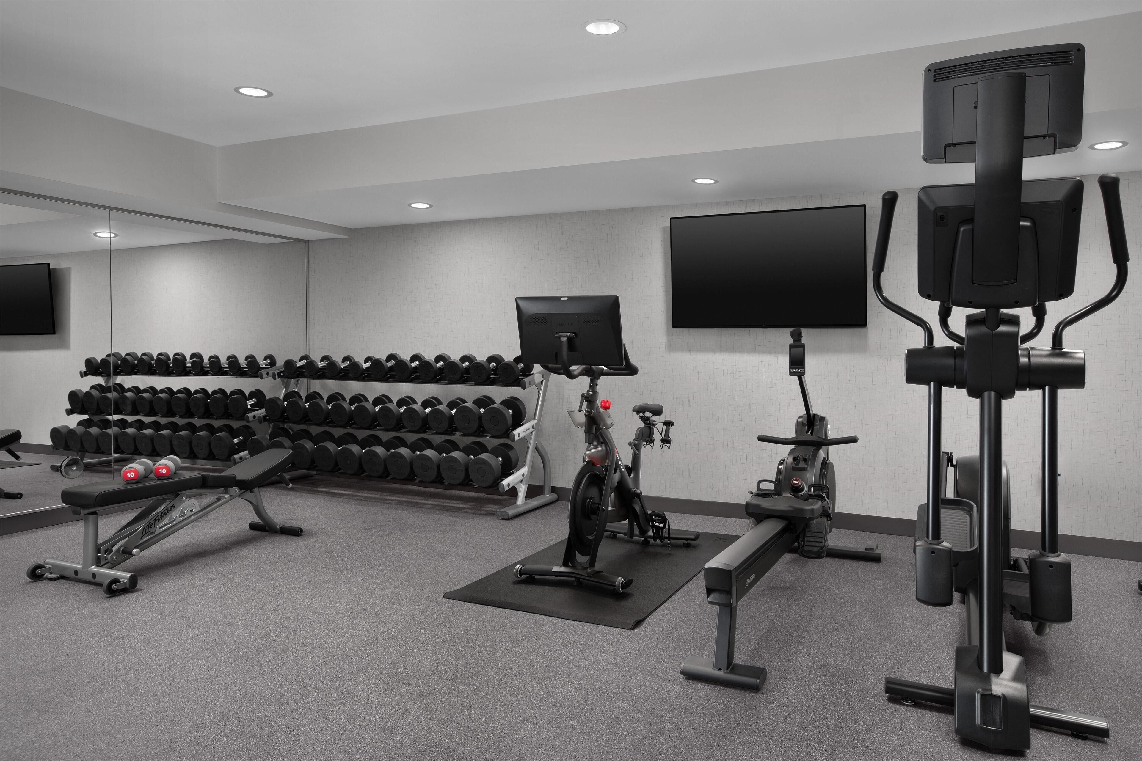 A gym with exercise equipment, dumbbells, and a television screen.