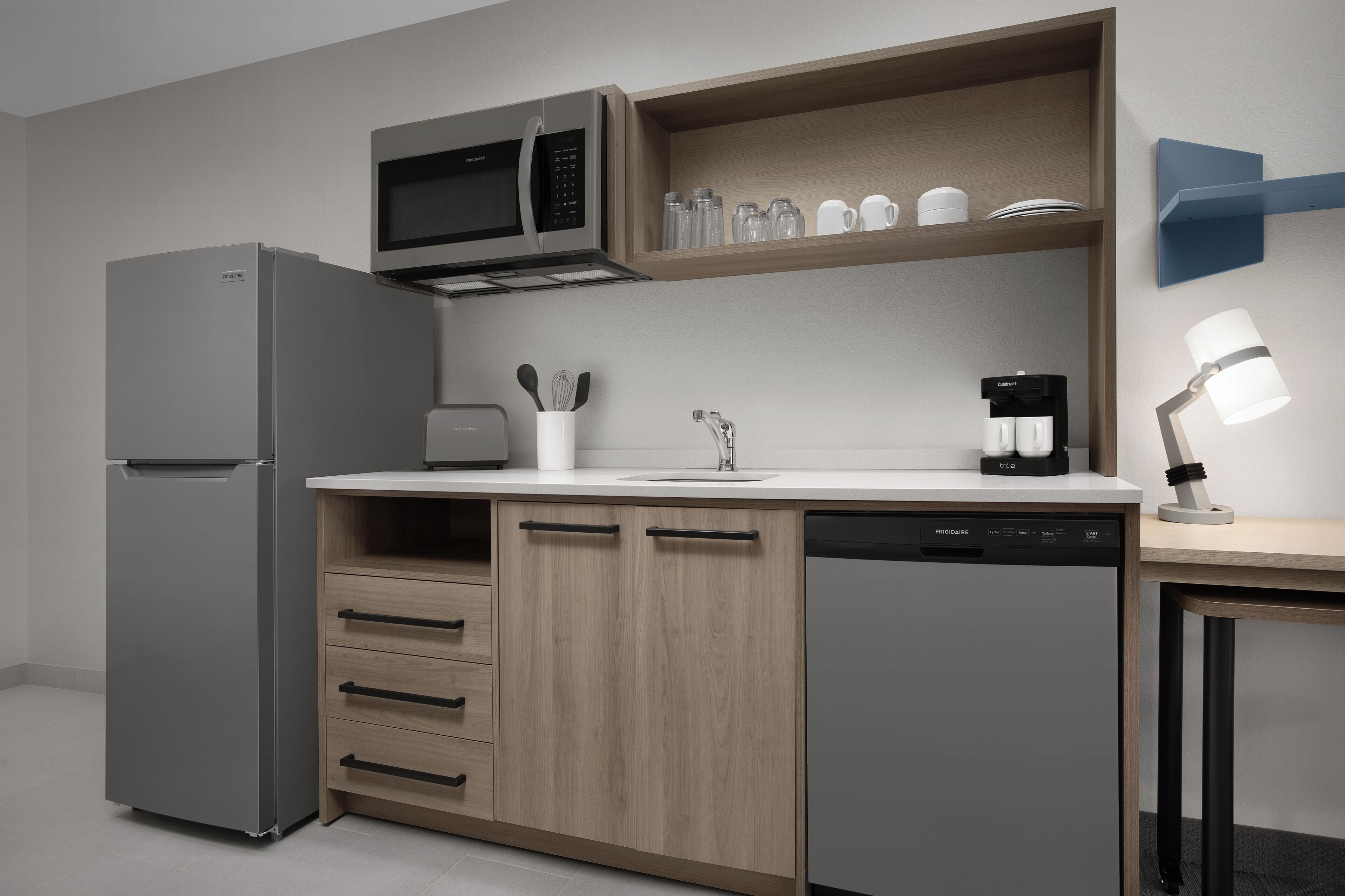 A compact kitchen with a refrigerator, microwave, coffee maker, and a built-in dishwasher.