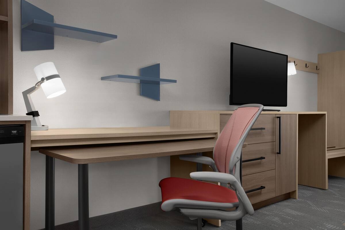 A modern office space with a desk, chair, television, and storage cabinets.