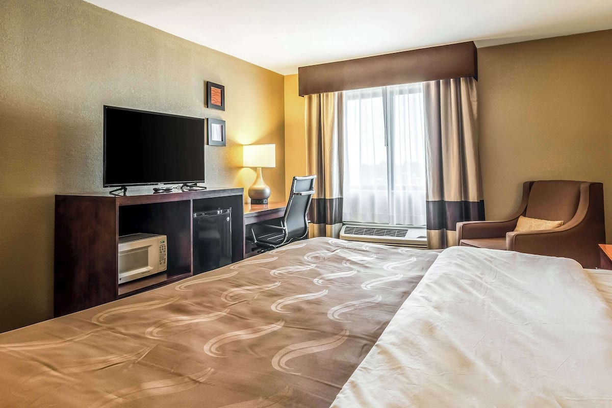 A hotel room with a bed, a desk with a computer, a TV, a lamp, and a chair.