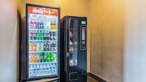 Un distributeur automatique avec un compartiment réfrigéré pour les boissons Coca-Cola et un autre distributeur, de couleur noire, placé à côté.