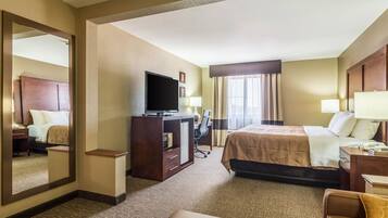 A hotel room with a bed, a desk with a computer, a TV, and a mirror.