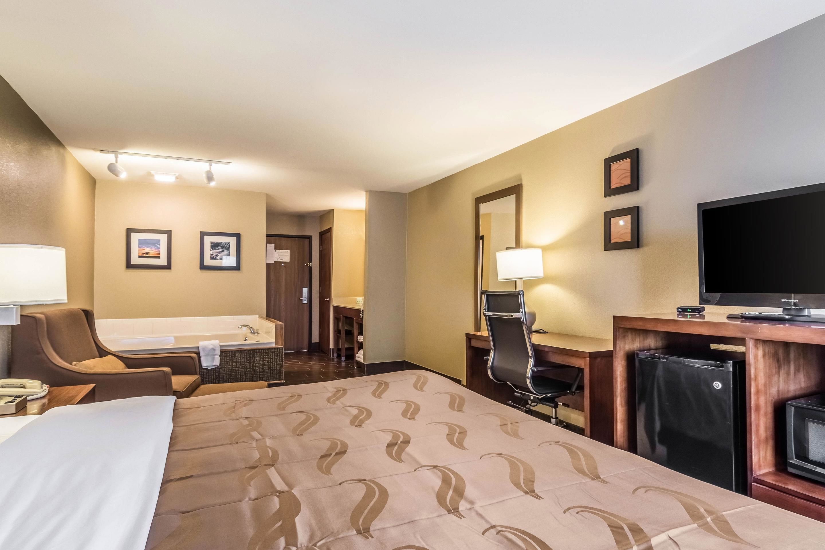 Una habitación de hotel con una cama, un escritorio, una silla, televisión y un baño a la vista.