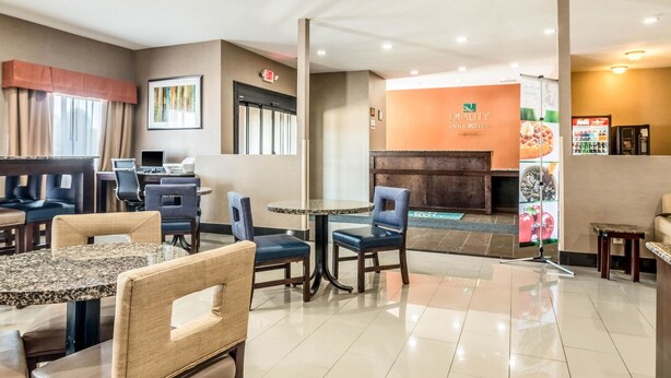 Un hall d’hôtel comprenant un comptoir d’accueil, un espace salon avec des tables et des chaises, et une enseigne indiquant « Quality Inn & Suites ».