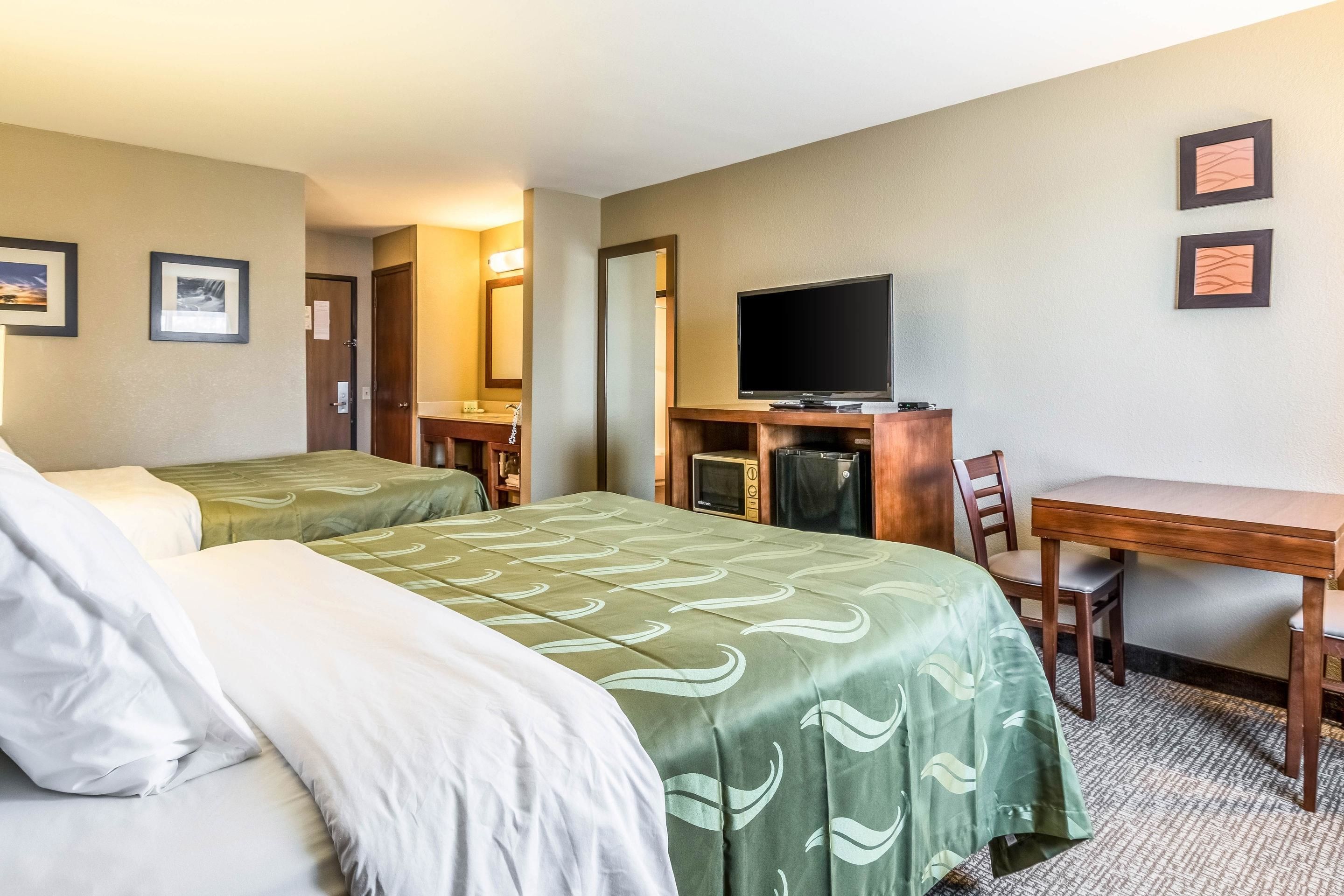 A hotel room with two beds, a desk, a television, and a mirror.