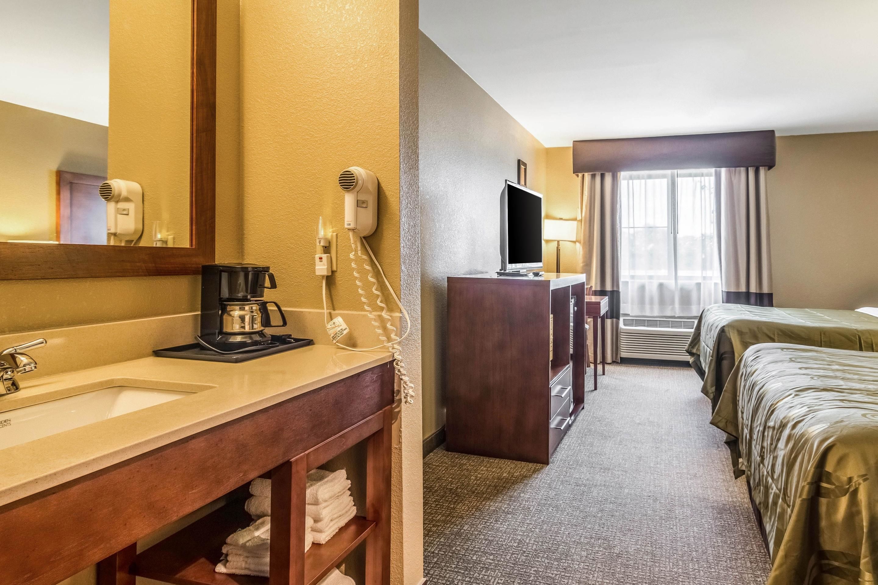 Une chambre d’hôtel équipée d’un lavabo, d’un miroir, d’un sèche-cheveux, d’une télévision et de deux lits.