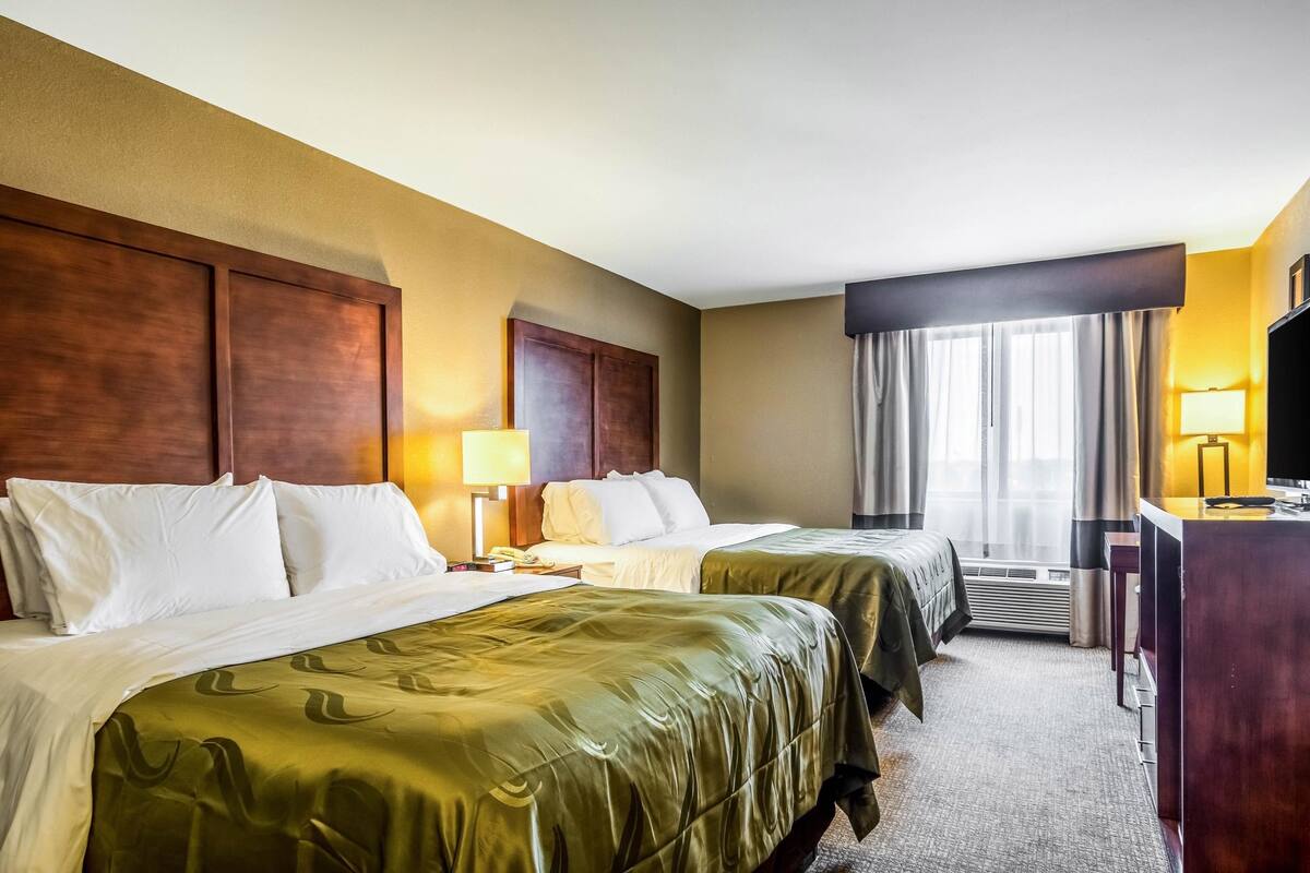 A hotel room with two beds, a desk, a TV, and a window with curtains.