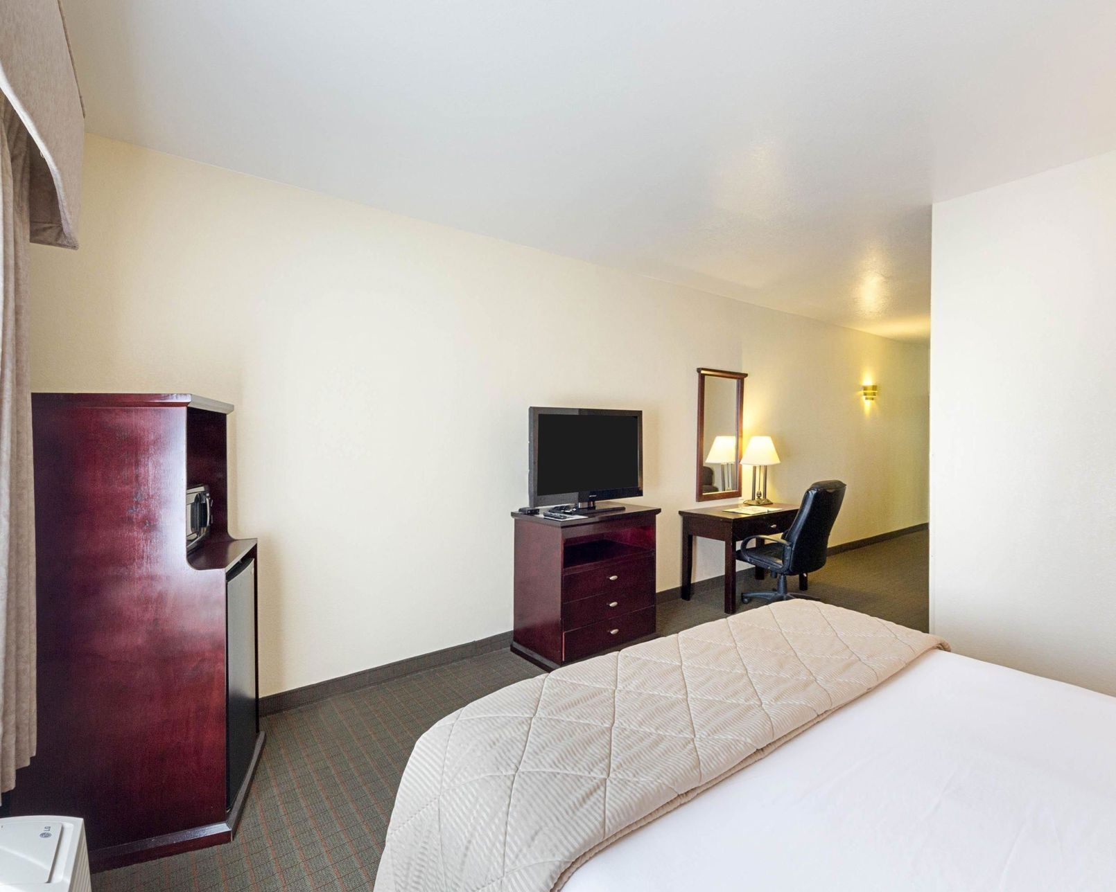 Habitación de hotel con cama, escritorio, silla, televisor, espejo y minibar.