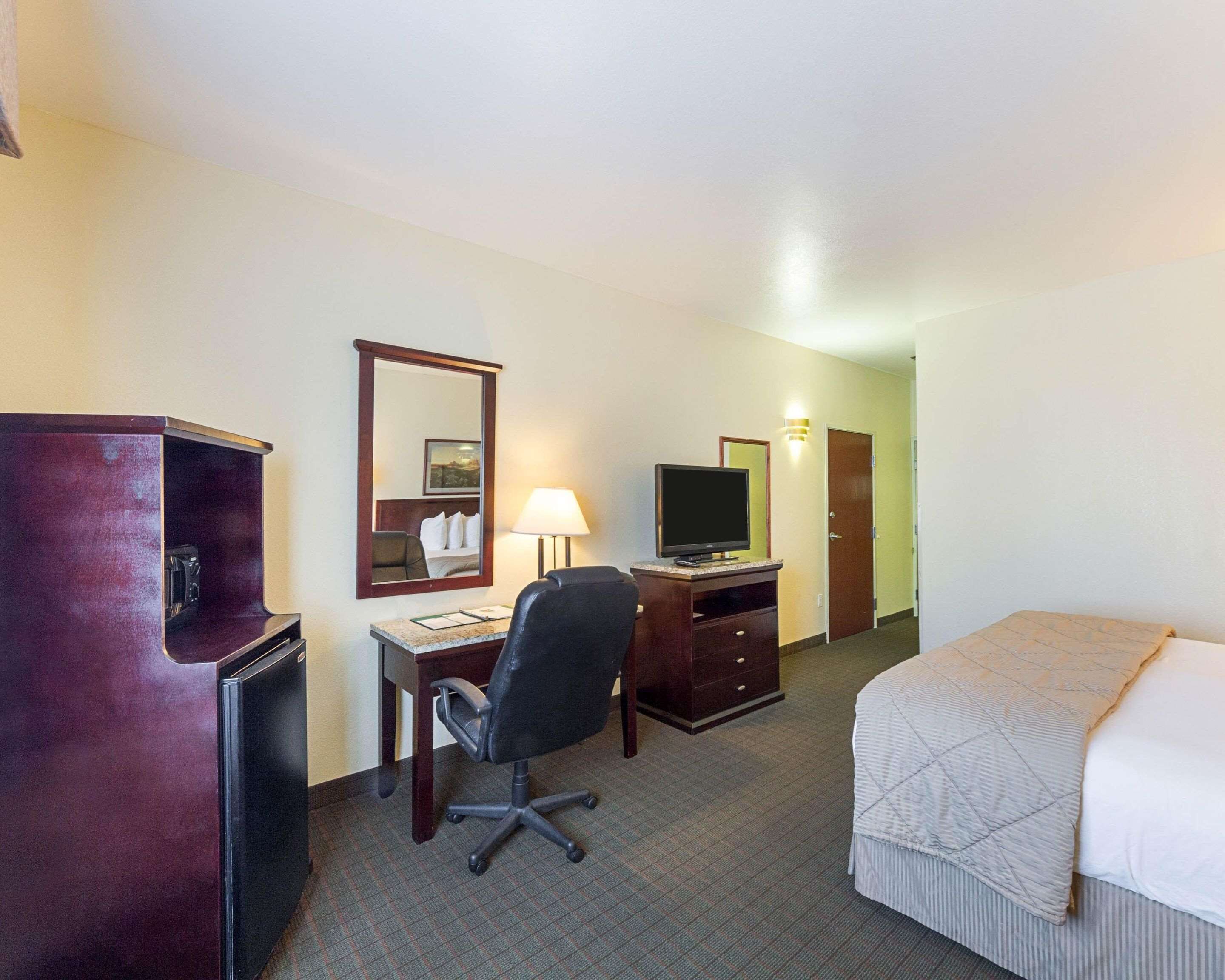 Una habitación de hotel con cama, escritorio, silla, televisor, espejo y armario.