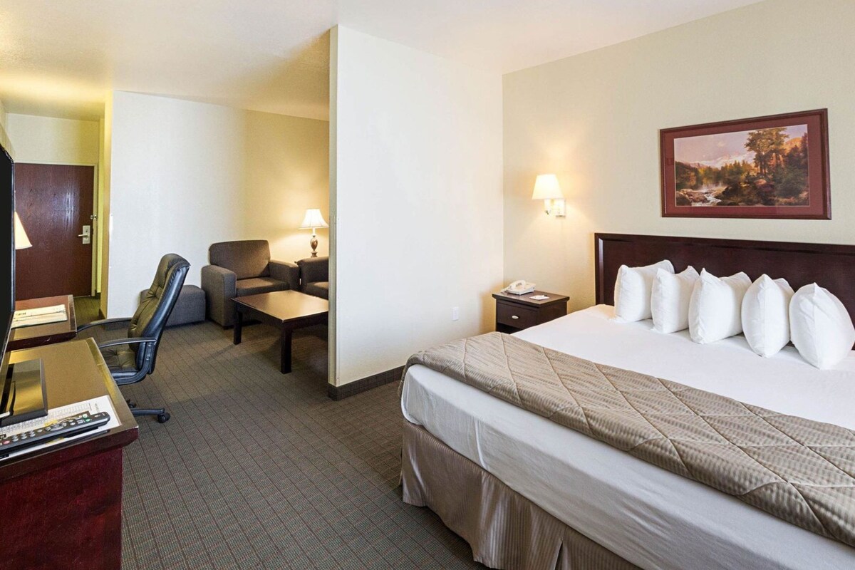 A hotel room with a bed, desk, chairs, and a painting on the wall.