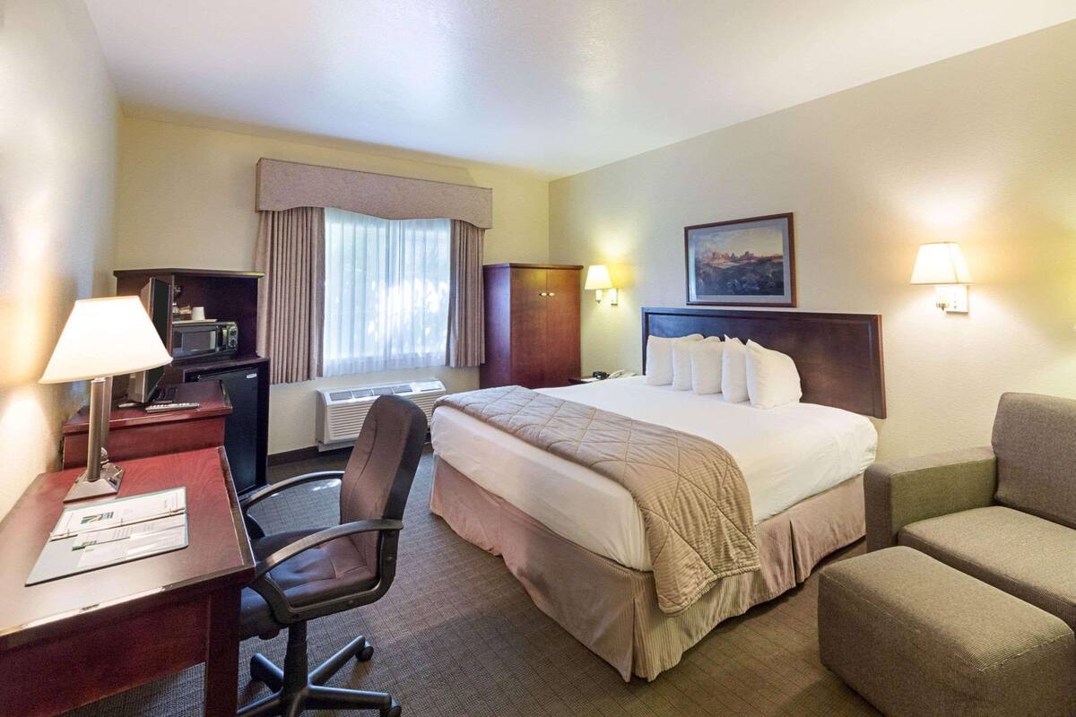 A hotel room with a bed, desk, chair, and a small kitchenette.