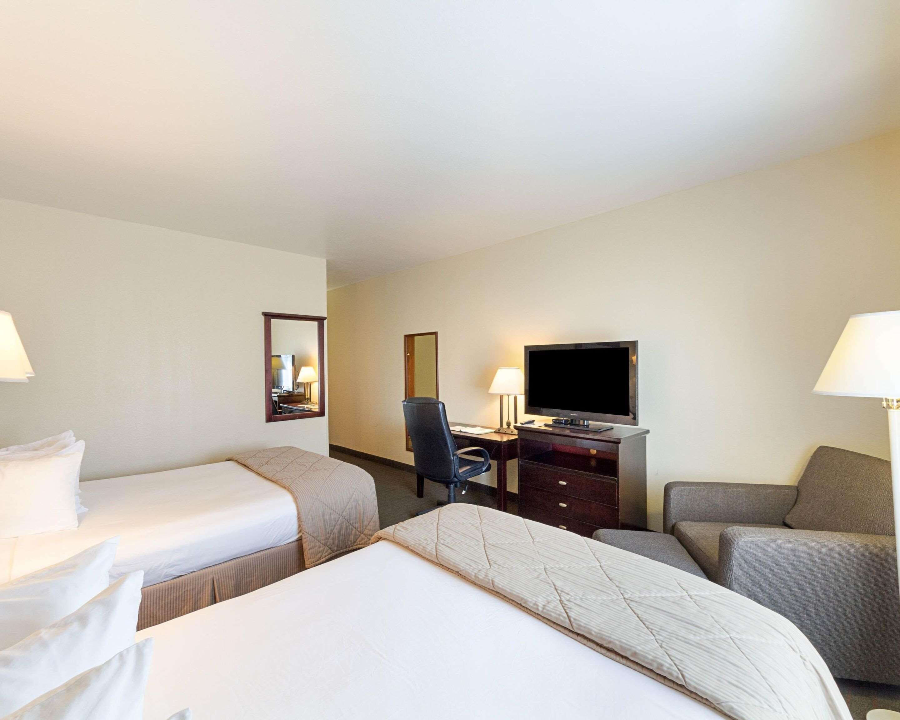 A hotel room with two single beds, a desk with a television, a chair, and two lamps.