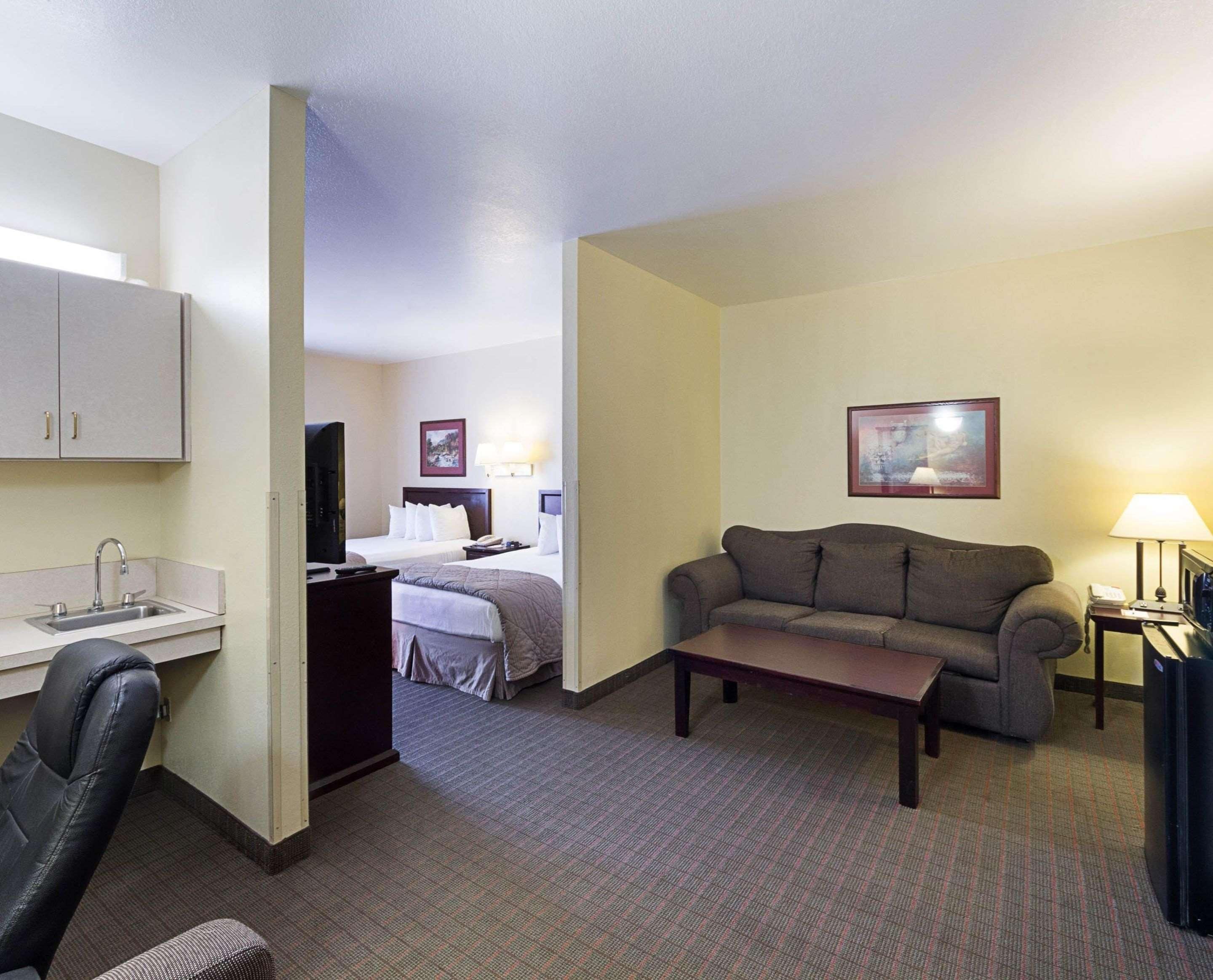 A hotel room with a kitchenette, a sofa, a small table, a desk, and a bed.