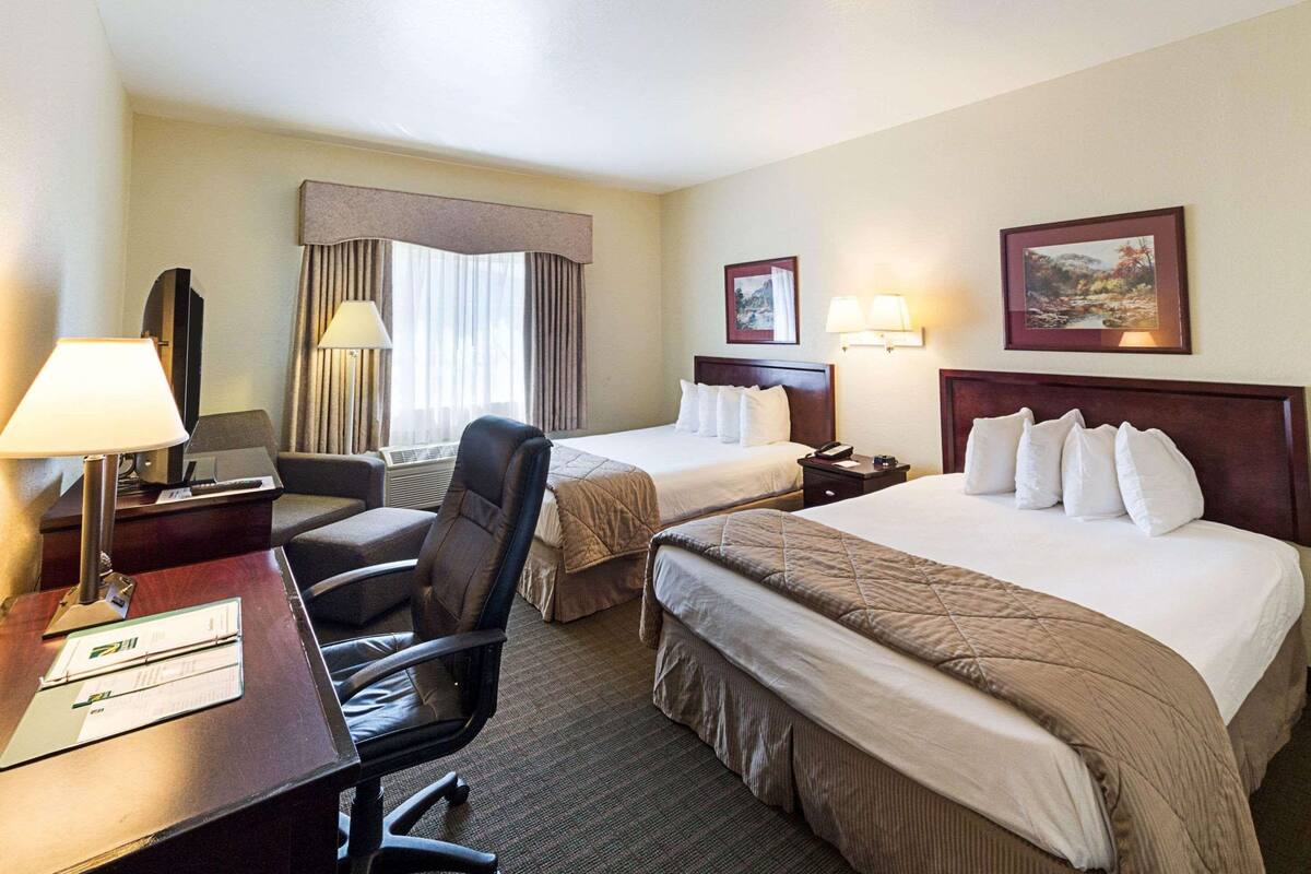 A hotel room with two beds, a desk with a chair, a TV, and a window with curtains.