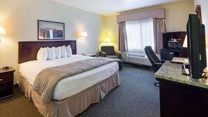 A hotel room with a large bed, a desk with a computer, a chair, a TV, and a window with curtains. - Quality Inn & Suites Kerrville (Kerrville)