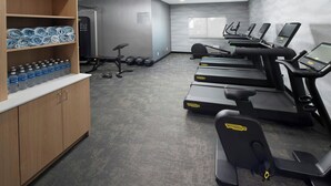 Ein Fitnessraum mit Laufbändern, Übungsbällen und Wasserflaschen auf Regalen.