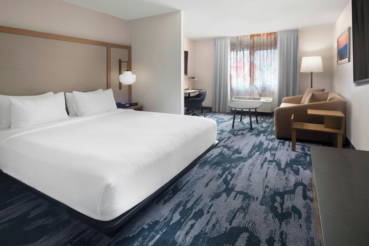 A hotel room with a large bed, a desk, a chair, a sofa, and a window with curtains.