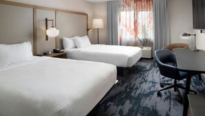 Ein Hotelzimmer mit zwei Betten, einem Schreibtisch, einem Stuhl, einer Lampe und einem Fenster mit Vorhängen.
