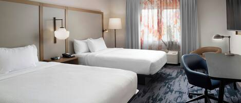A hotel room with two beds, a desk, a chair, a lamp, and a window with curtains.
