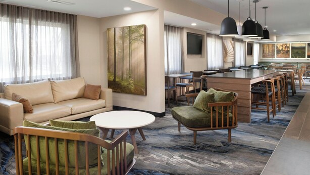 Eine Hotelhalle mit einer Couch, Sesseln, einem runden Tisch, einer Bar und einem großen Gemälde.