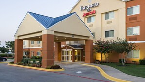 Ein Fairfield Inn Marriott Hotel mit überdachter Eingangspartie, Parkplatz und einer begrünten Fläche mit Blumen.
