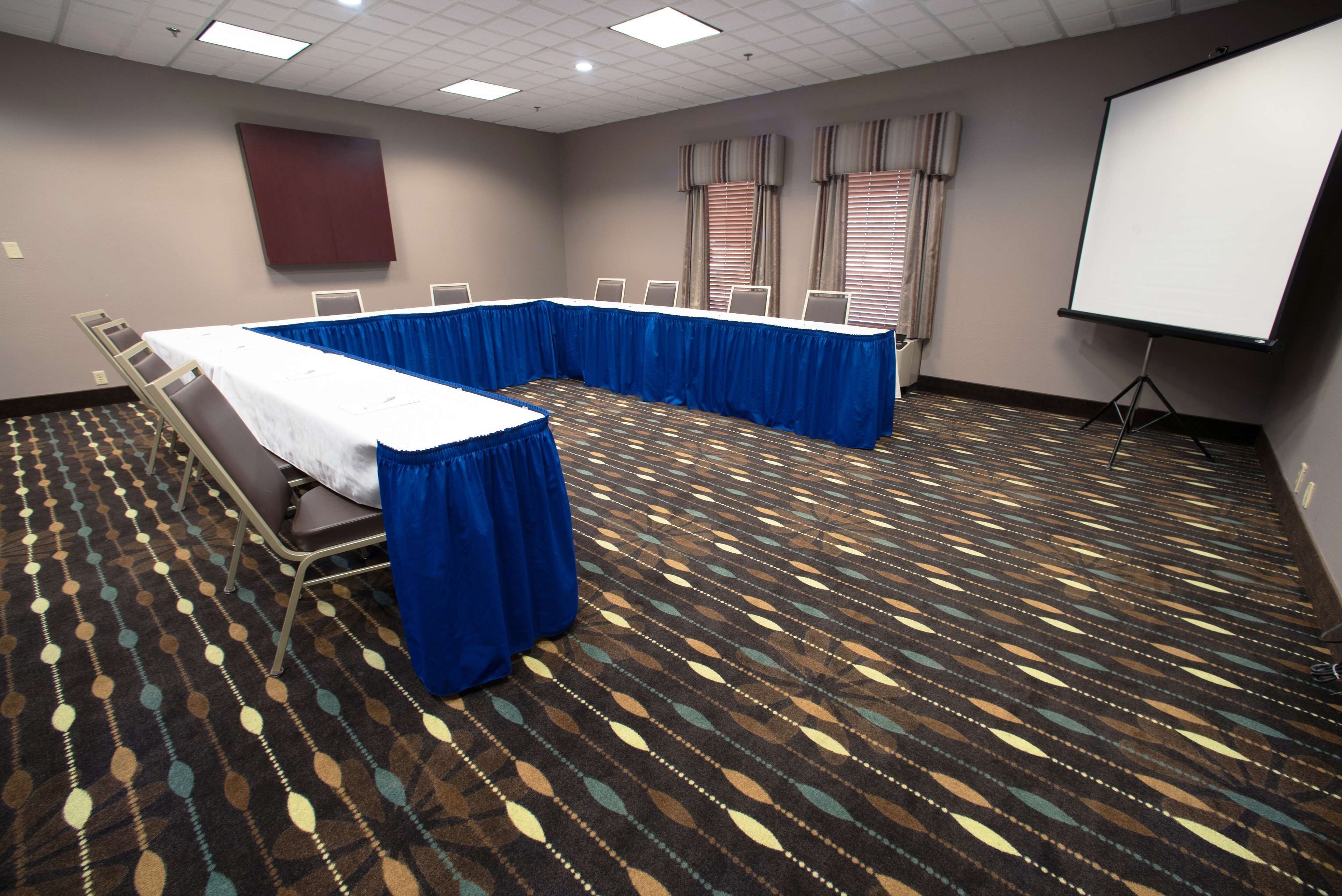 A conference room with a long table, blue tablecloths, and a projector screen.