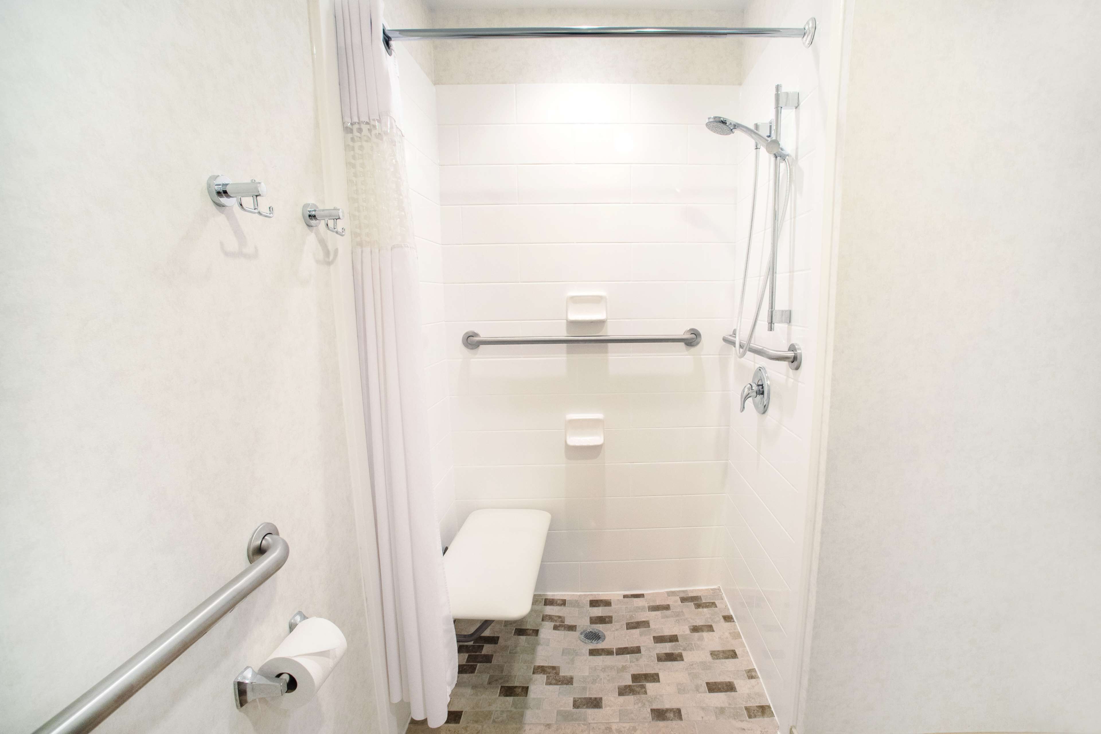 Ein kleines, weiß gefliestes Badezimmer mit Dusche, Toilette und einer Sitzbank.