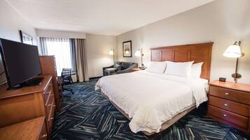 A hotel room with a large bed, a desk with a computer, a TV, a chair, and a lamp.