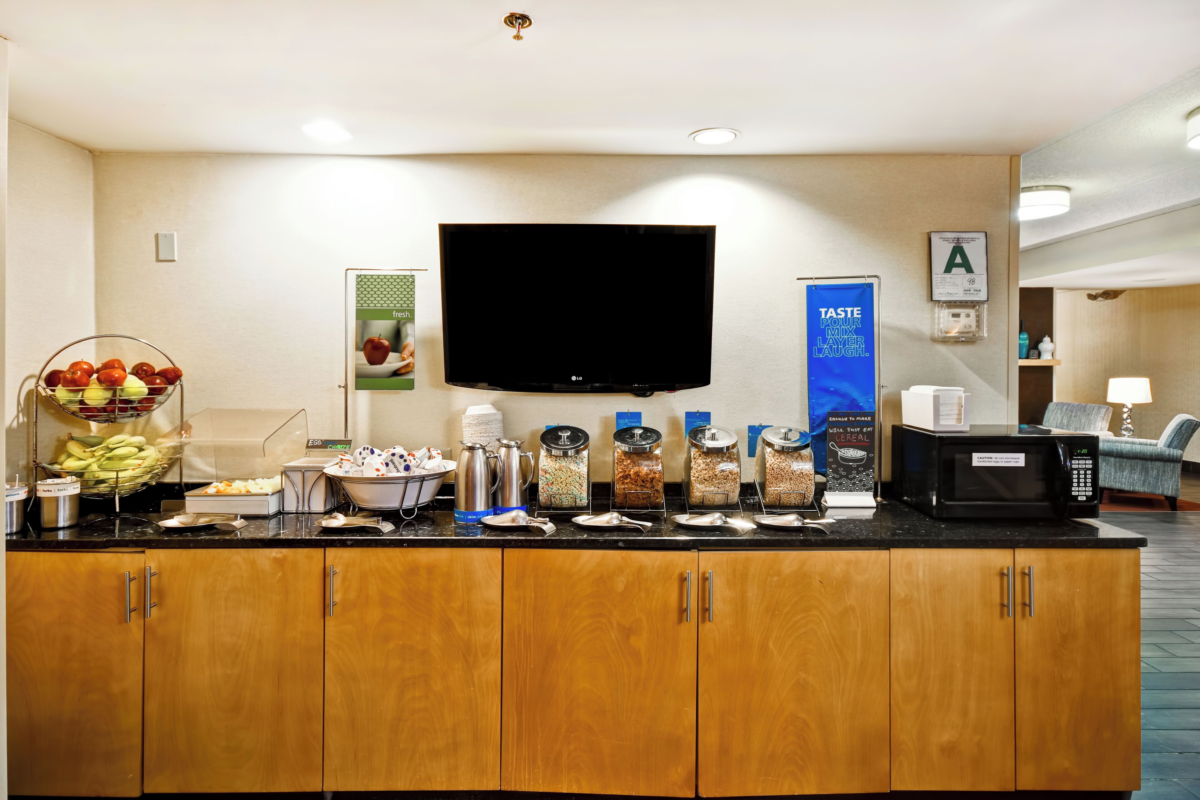 Zona de recepción de un hotel con un televisor de pantalla plana, un frutero y varios recipientes de comida sobre una barra.