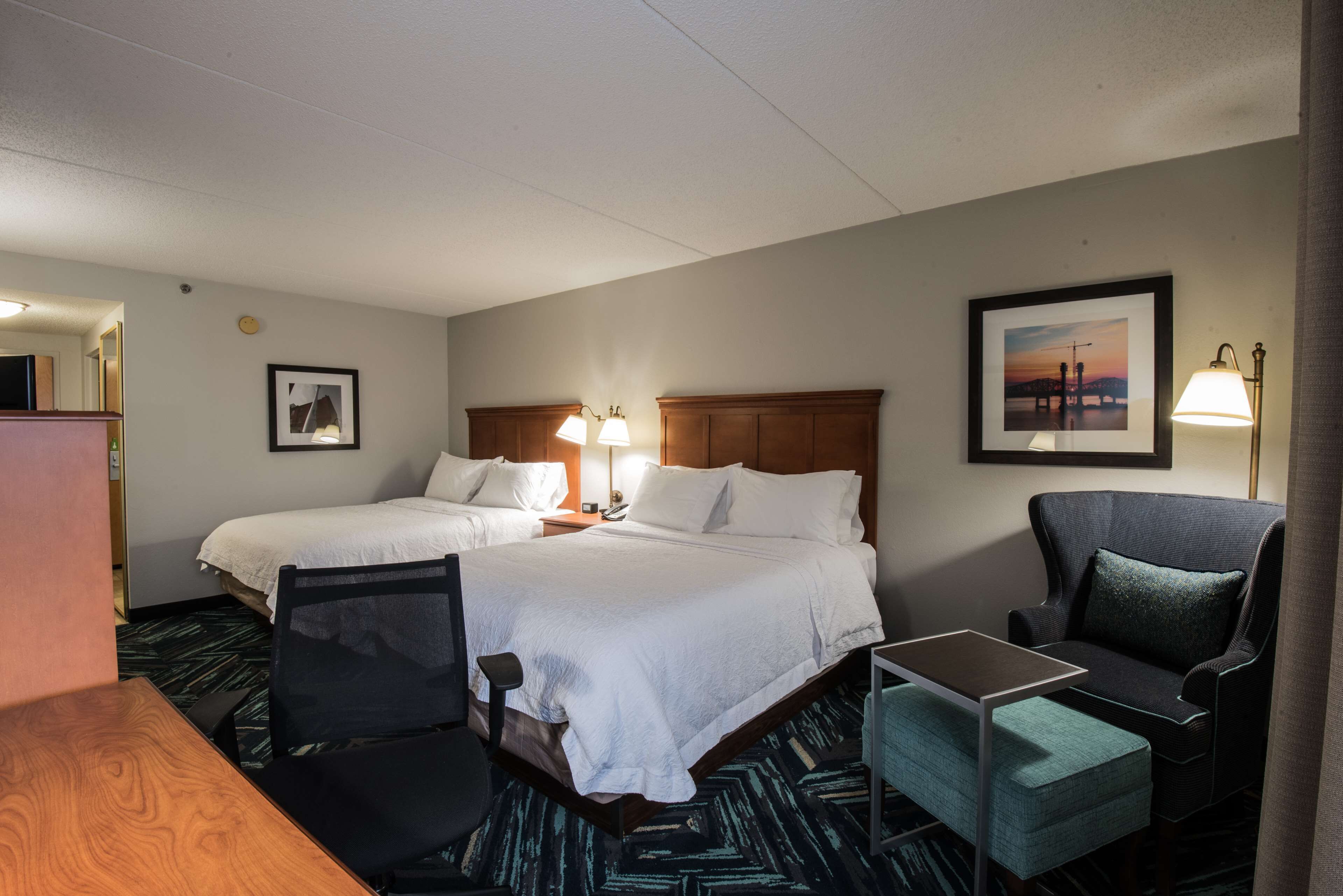 A hotel room with two beds, a desk, a chair, and a small table.