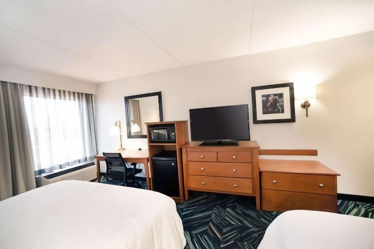 Une chambre d’hôtel avec deux lits, un bureau, une télévision et une commode.