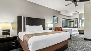 Una camera d'albergo con un letto grande, una scrivania con lampada, una sedia, un tavolino da trucco con specchio e una ventola a soffitto.