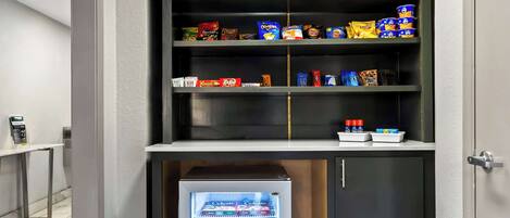 Una kitchenette compacta con un refrigerador lleno de bocadillos y un congelador debajo.